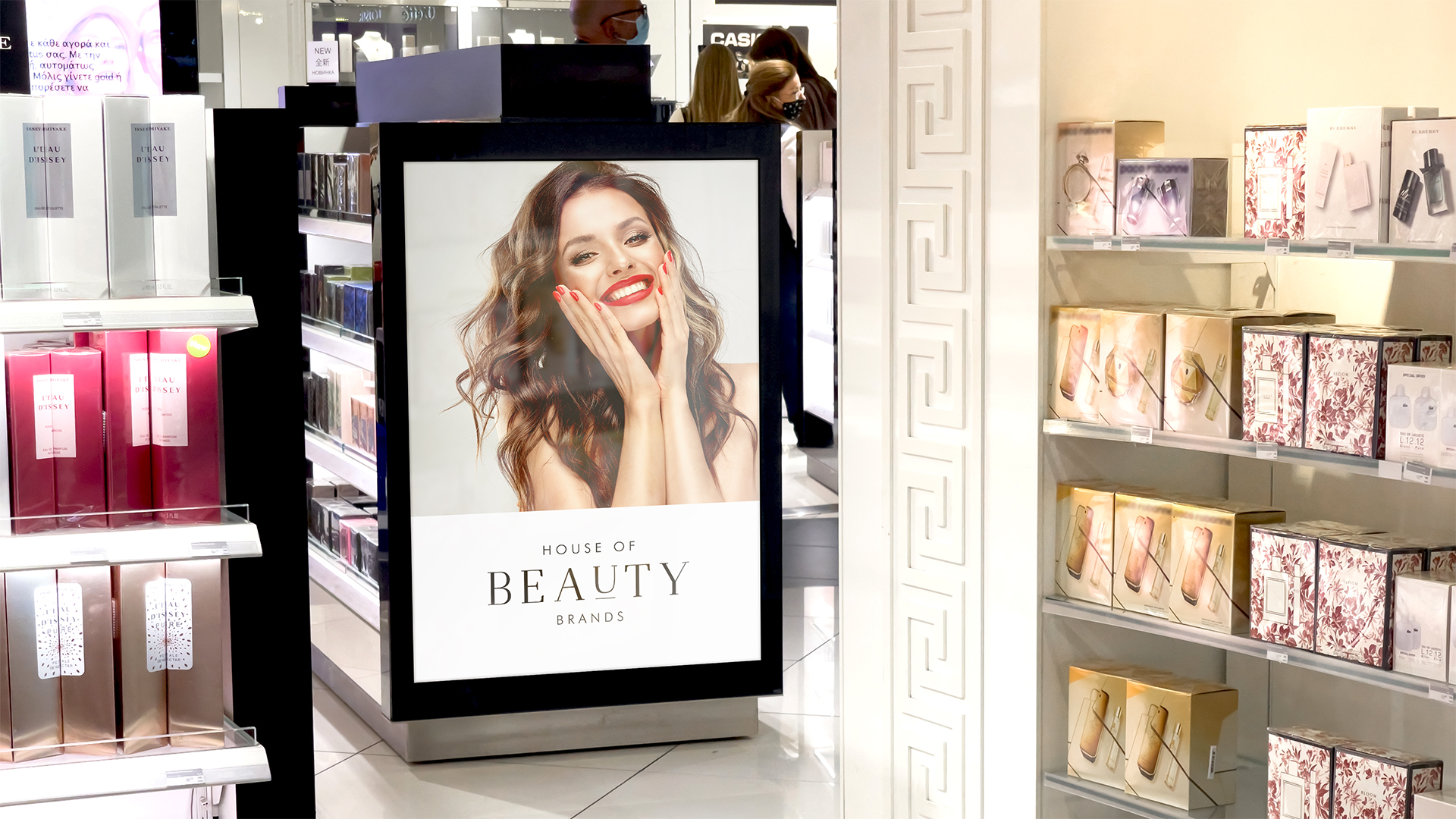 House Of Beauty Brands - plakat A3 pomiędzy pólkami sklepu kosmetycznego, na plakacie młoda uśmiechnięta kobieta, poniżej logo House of Beauty Brands